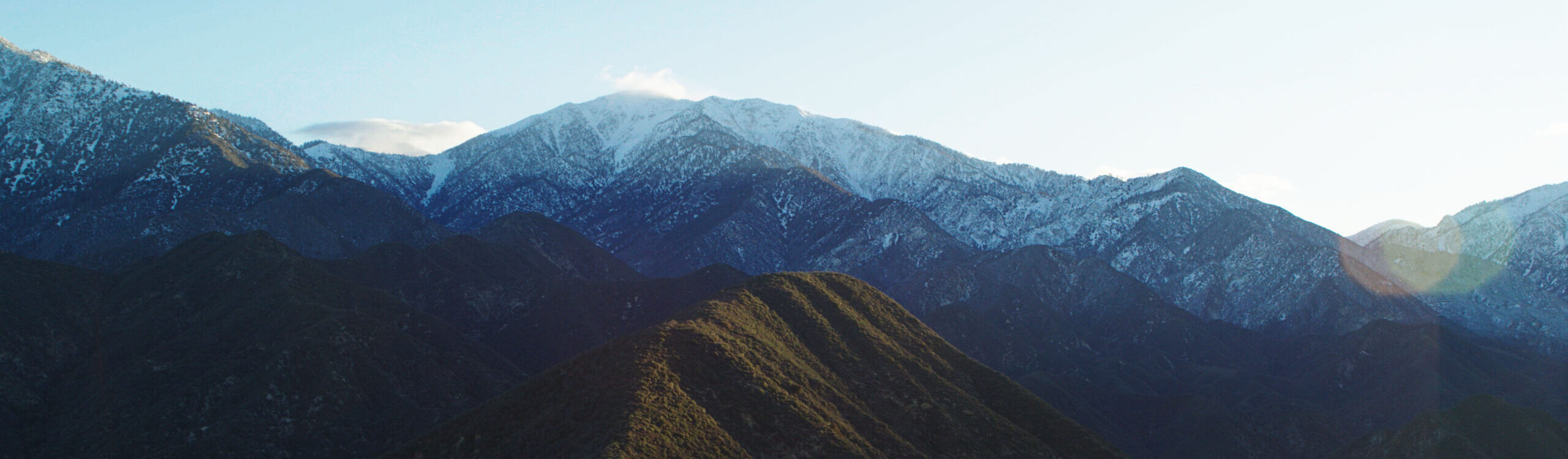 Witness the serene beauty of sunrise at Mount Baldy, with snow adorning its peaks, the wind blowing snowflakes, and a hint of a lens flare as the sun rises.