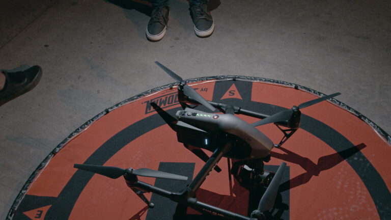 The DJI Inspire 2 drone rests on a landing pad, freshly equipped with a new set of batteries and ready for action on the set of Lash the Movie. The scene is set for capturing dynamic police car sequences, showcasing the precision and readiness of the AMK Films team.