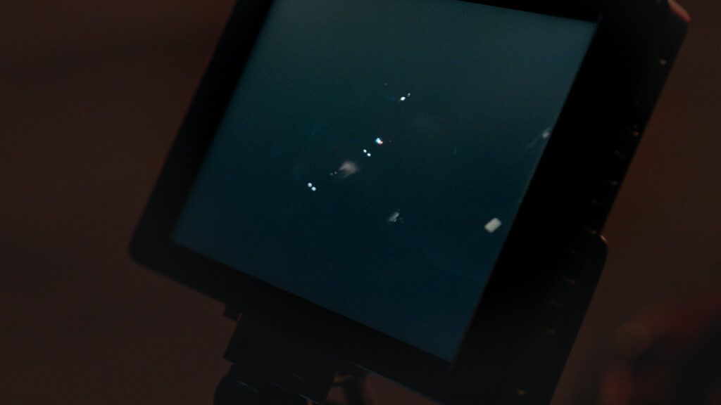 A behind-the-scenes shot of the crew reviewing the last take on a monitor during the filming of Lash the Movie. The intense police car chase scene is displayed, showcasing the precision and detail captured by the AMK Films team.