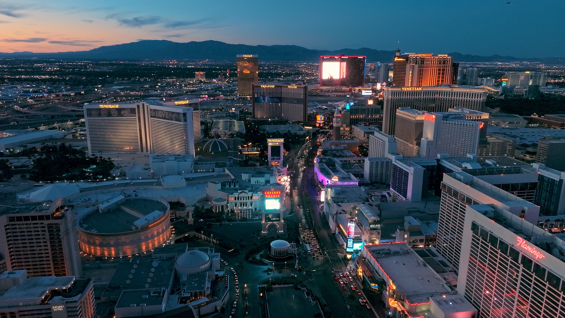 A beautiful shot of the Las Vegas Strip at sunset, featuring landmarks like the Mirage, Caesars Palace, Flamingo, Venetian, Bellagio, and Treasure Island, with the mountains in the background.